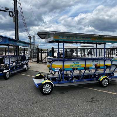 Two pedal-powered multi-seat vehicles parked in a lot under a cloudy sky.