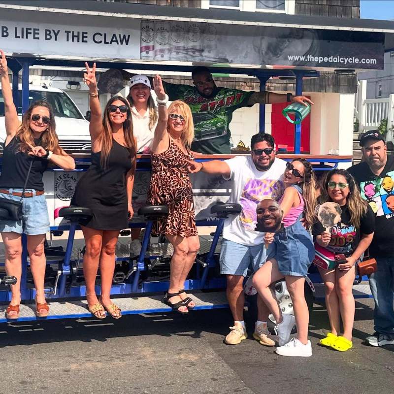 Group of people posing together by a pedal-powered vehicle with a White Claw advertisement.