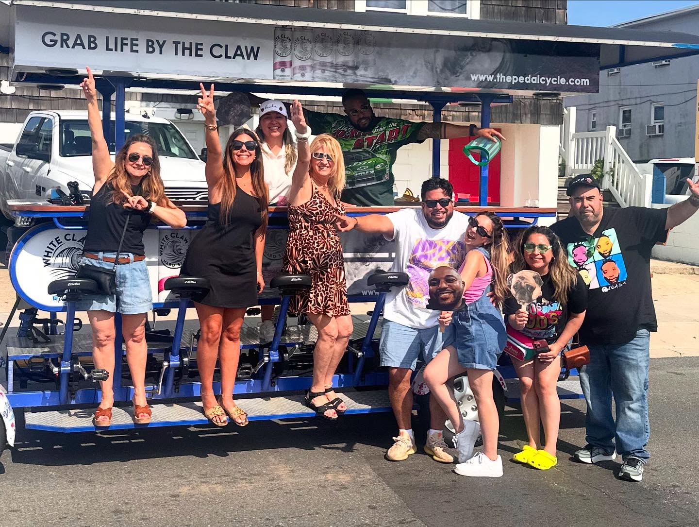Group of people posing in front of a pedal bar with 'Grab Life by the Claw' banner.
