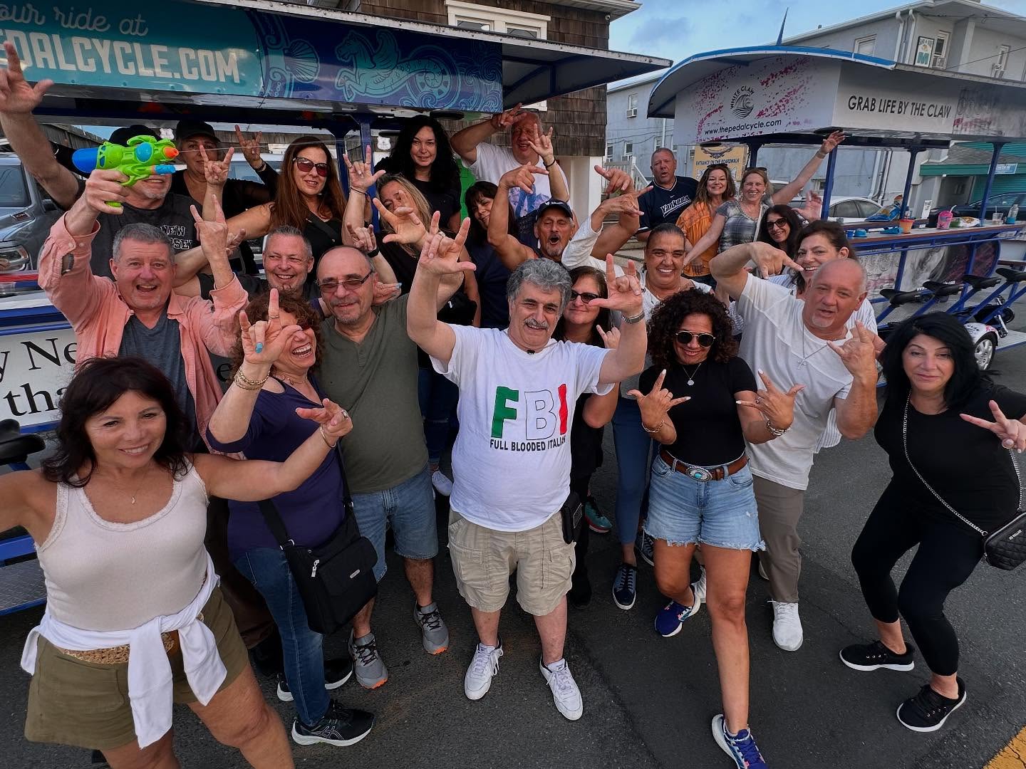 Group of people posing happily with various hand signs in front of a party bike on a street.
