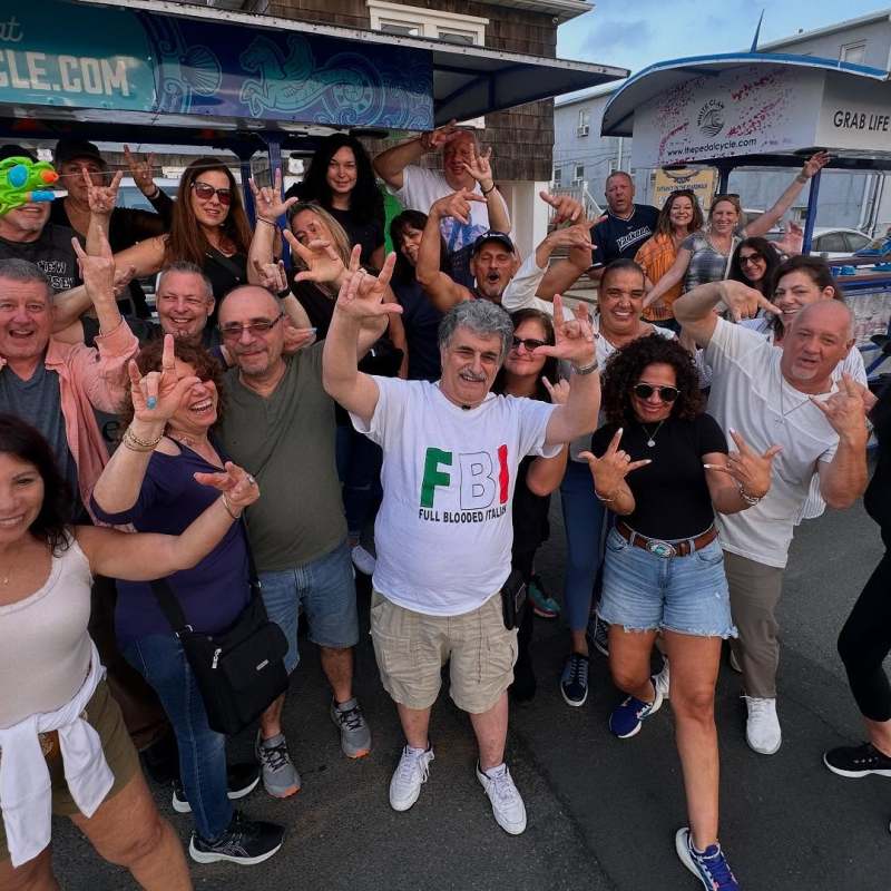 Group of people posing happily with various hand signs in front of a party bike on a street.