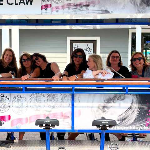 Seven women smiling on a pedal pub with White Claw branding.