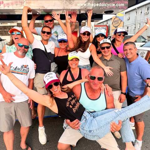 Group of joyful people posing outside with one person being lifted in the front.