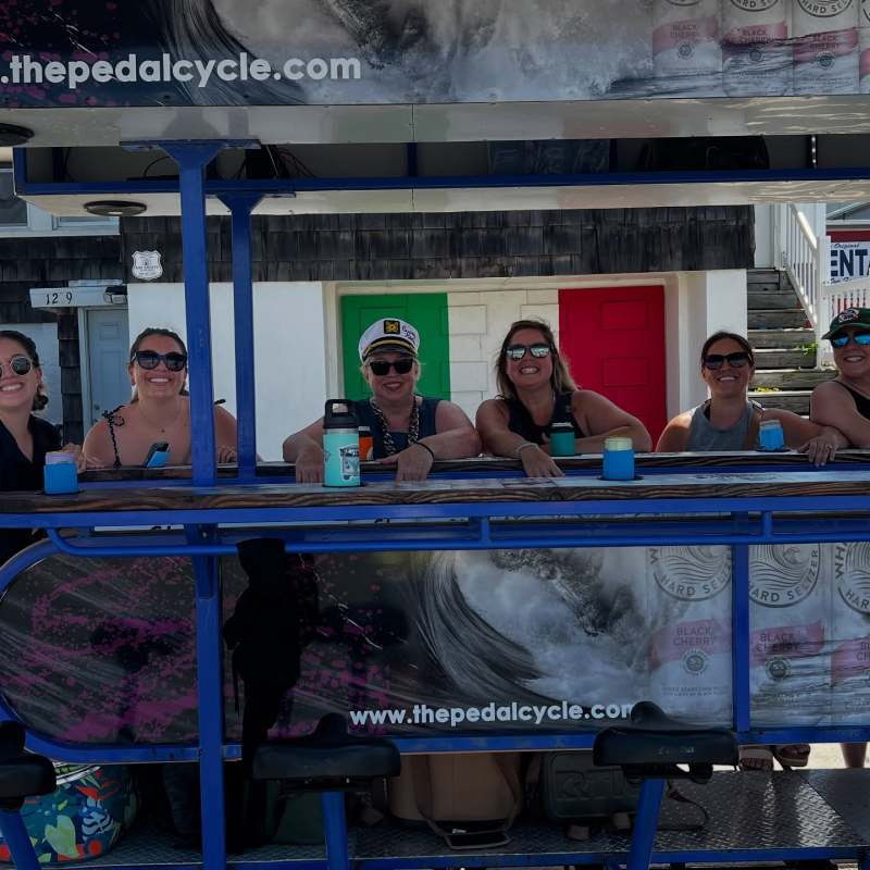 Group of people on a pedal cycle with advertisements, smiling and enjoying a sunny day.