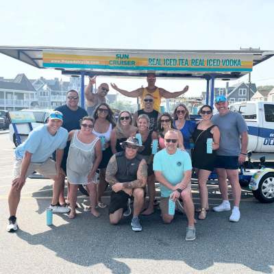 Group of people posing in front of pedal cycle with 'Sun Cruiser' sign.