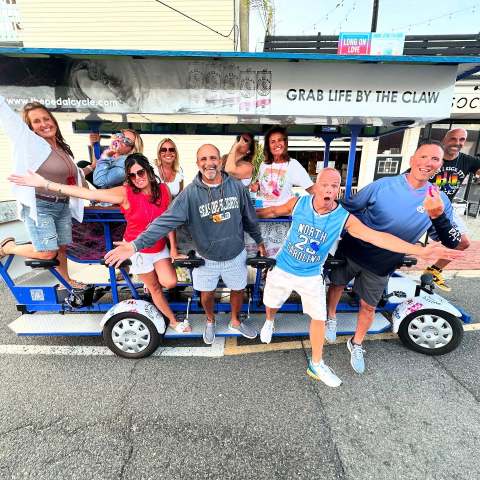 Group of people having fun on a pedal-powered vehicle on a street, smiling and posing energetically.
