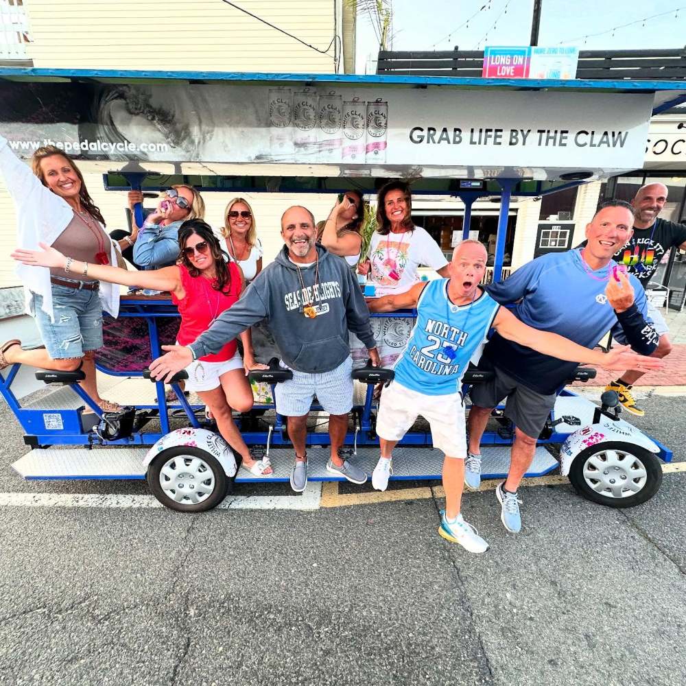 Group of people having fun on a pedal-powered vehicle on a street, smiling and posing energetically.