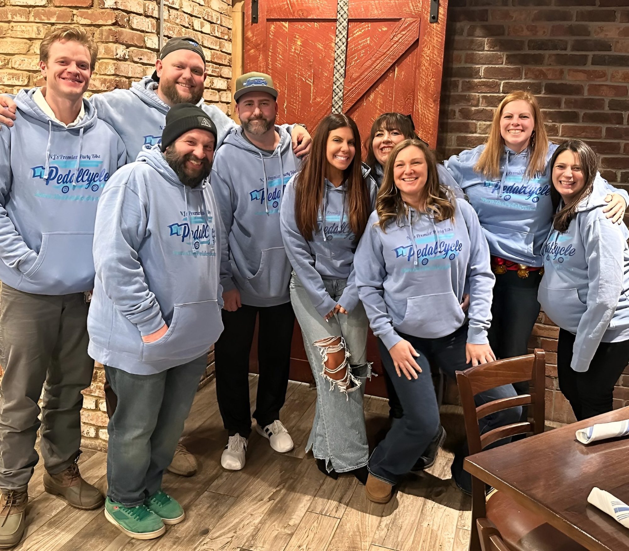Group of people in matching light blue hoodies posing indoors with brick walls.