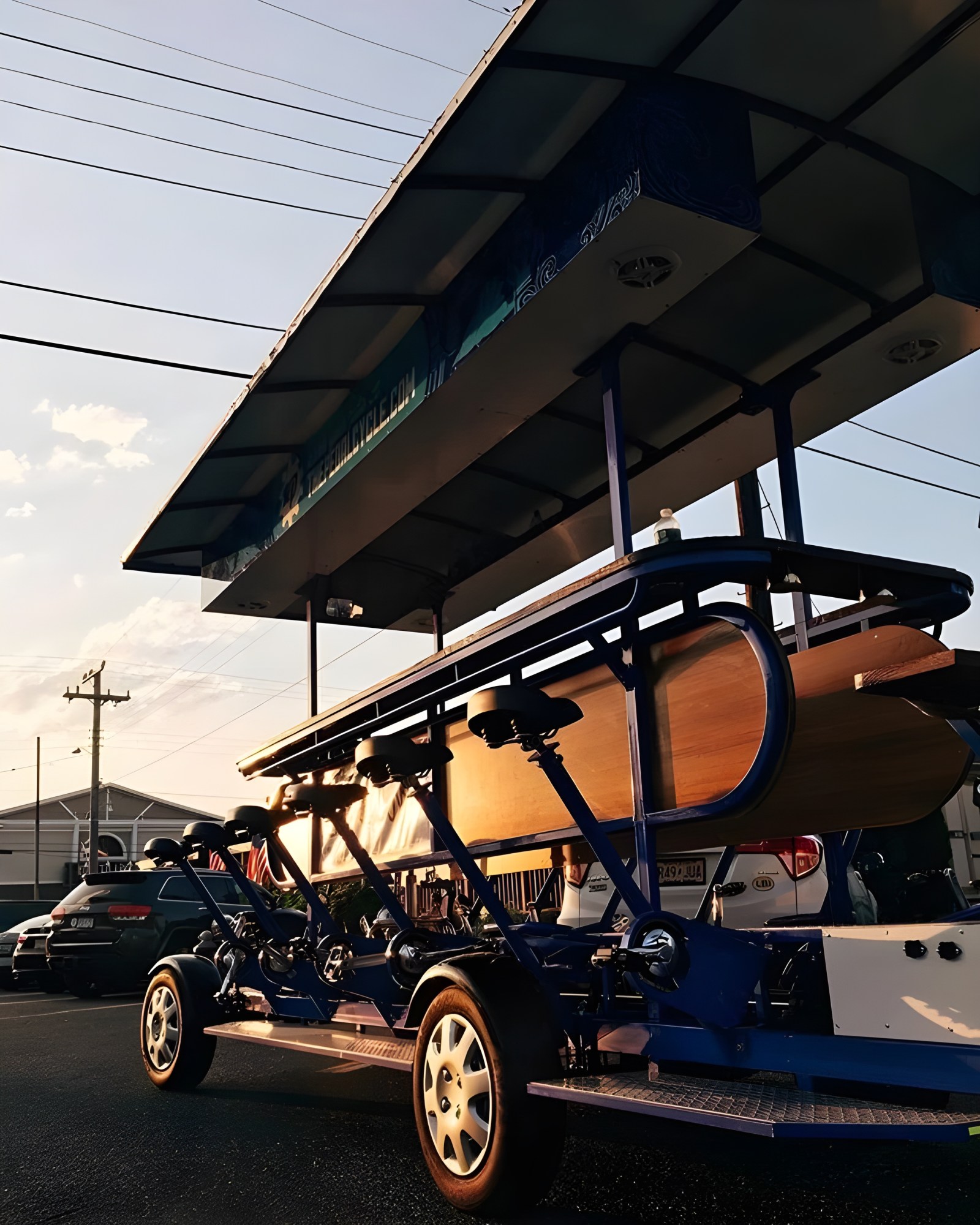 Large trolley bike with bar seating parked on street under evening sky.